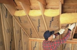 Technician installing batt insulation in an unfinished ceiling.