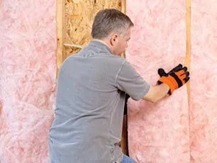 Pink fiberglass insulation being installed inside a wall by a technician in a gray shirt.