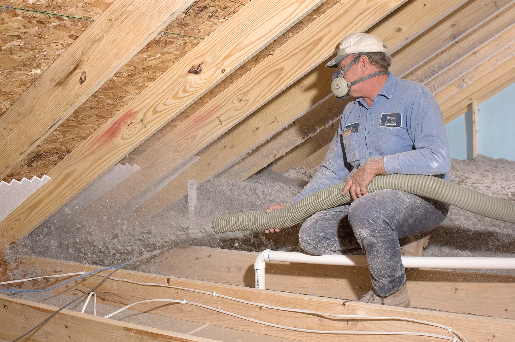 Technician blowing loose-fill insulation into an unfinished attic.