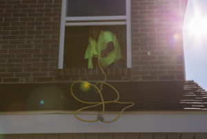 Insulation removal, technician stretching yellow cord out a second-story window of a brick home.